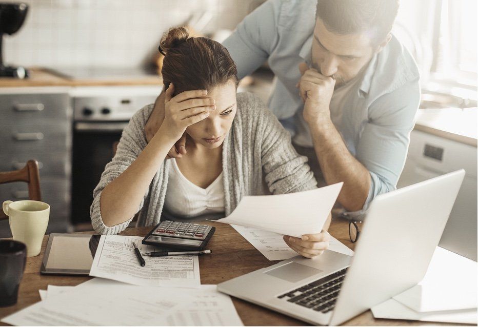 Un couple examine des factures à la table de la cuisine, l'air stressé.