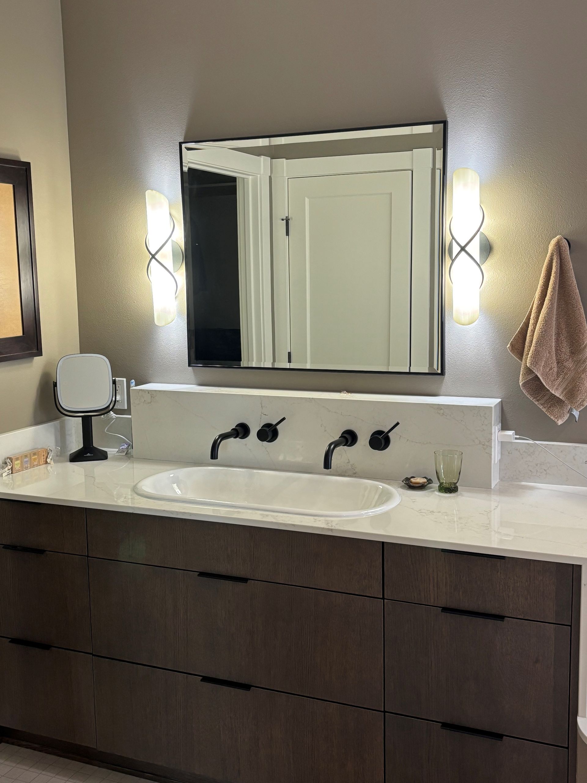 Bathroom with a dark wood vanity, white countertop, oval sink, and a large mirror with sconces.