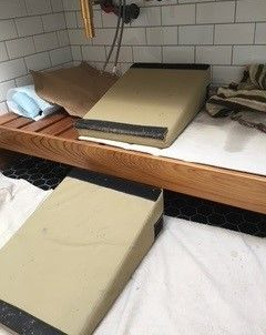 Two tan foam ramps on a wooden platform covered with a white cloth, near a tiled wall.