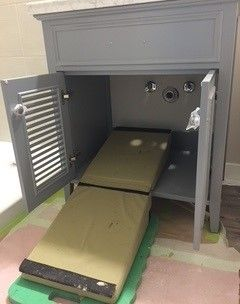 Open bathroom vanity cabinet with a pull-out shelf. Gray cabinet, doors open, beige shelf extended.