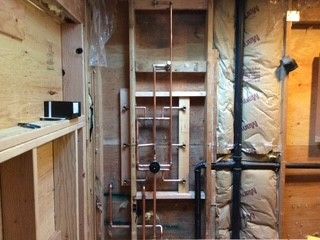 Copper plumbing pipes in a wooden wall, with black pipe on the right and insulation visible.
