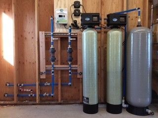 Water treatment system installed on a wooden wall with tanks, pipes, and control panels.