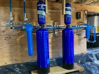 Blue water filtration system with tanks and pipes in a basement setting.