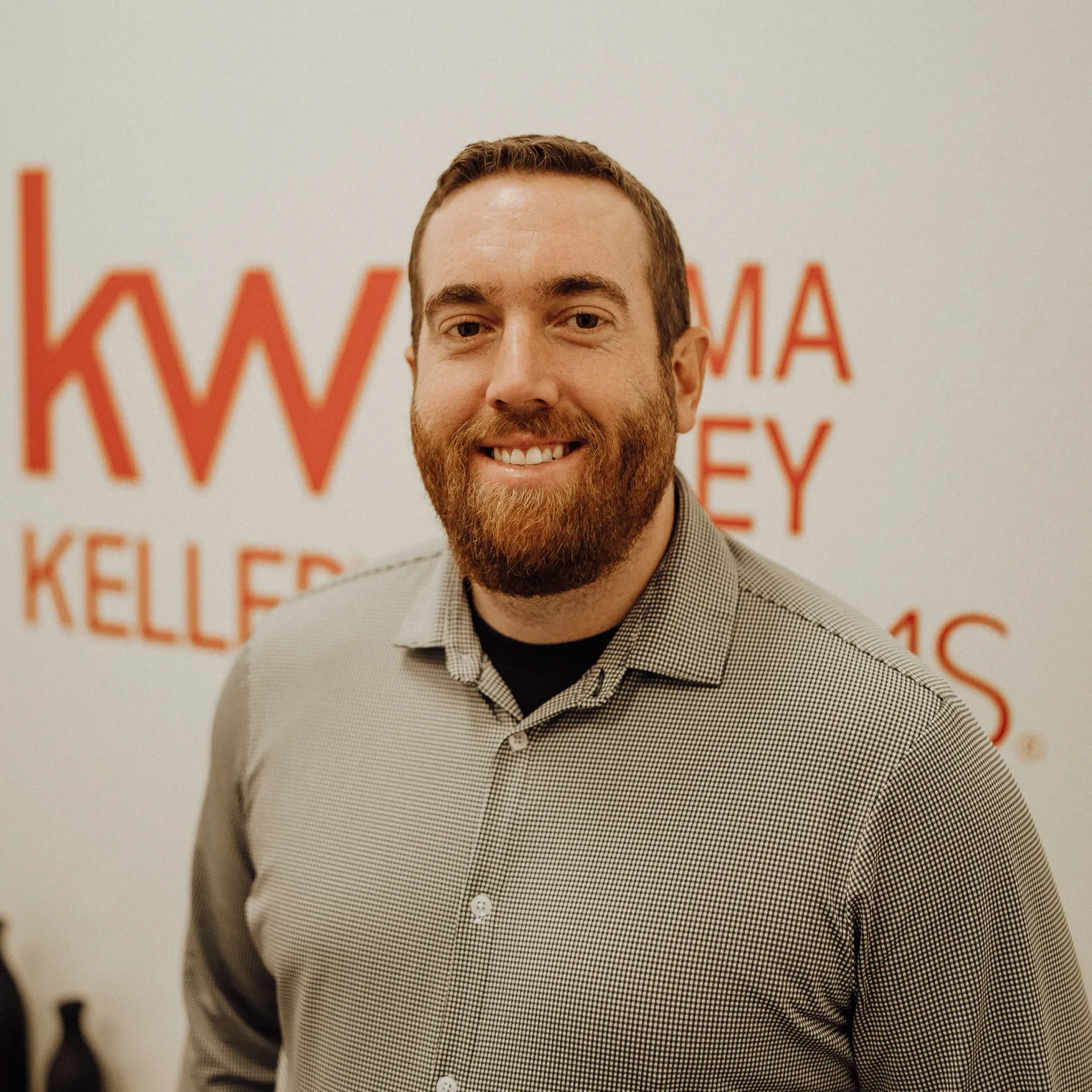 A man with a beard is standing in front of a wall with the letters kw on it.