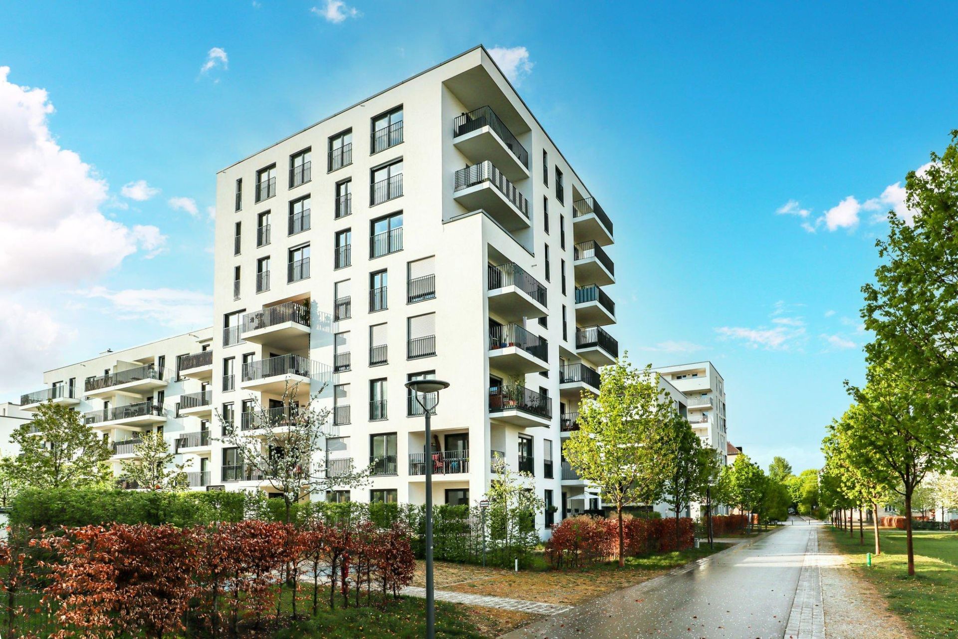 A large white apartment building is surrounded by trees and bushes in a residential area.