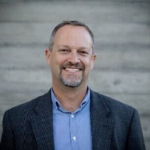 A man in a suit and blue shirt is smiling for the camera.