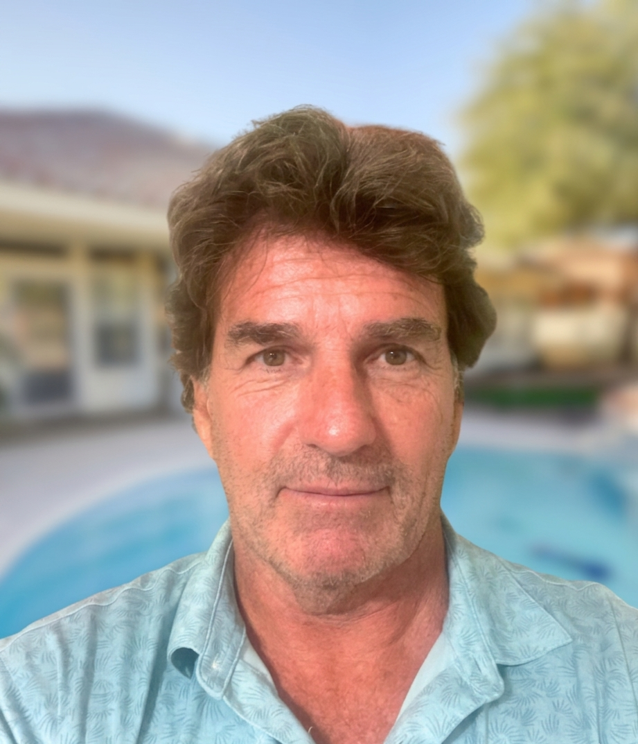 Man with brown hair and light blue shirt in front of a blurred pool and house.