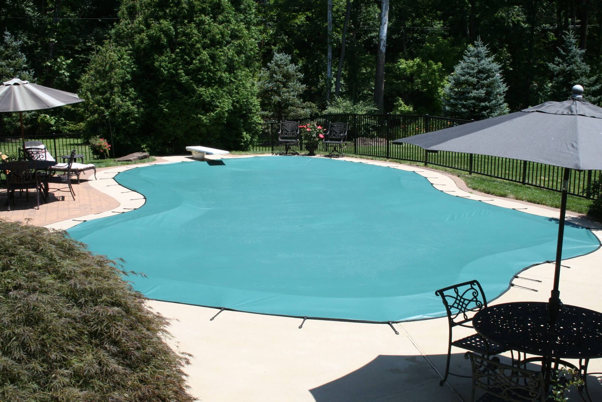 Teal pool cover over a backyard pool, surrounded by concrete and trees.