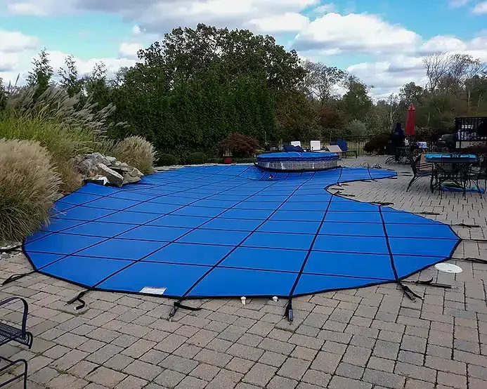 Blue pool cover on a brick patio, covering a pool. Trees and sky in the background.