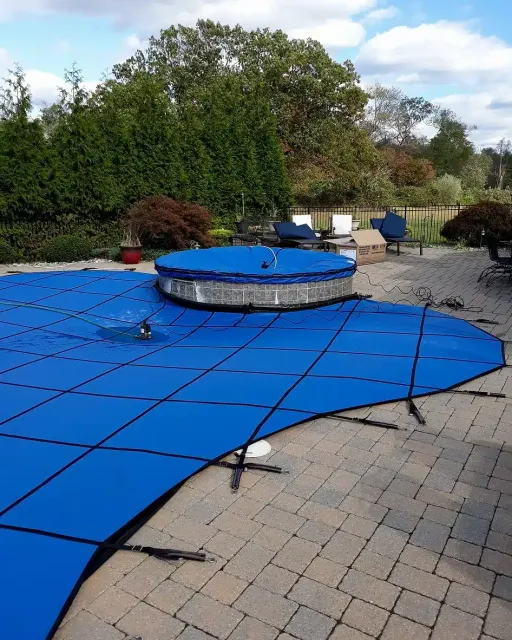 Blue pool cover over a circular above-ground pool on a brick patio.