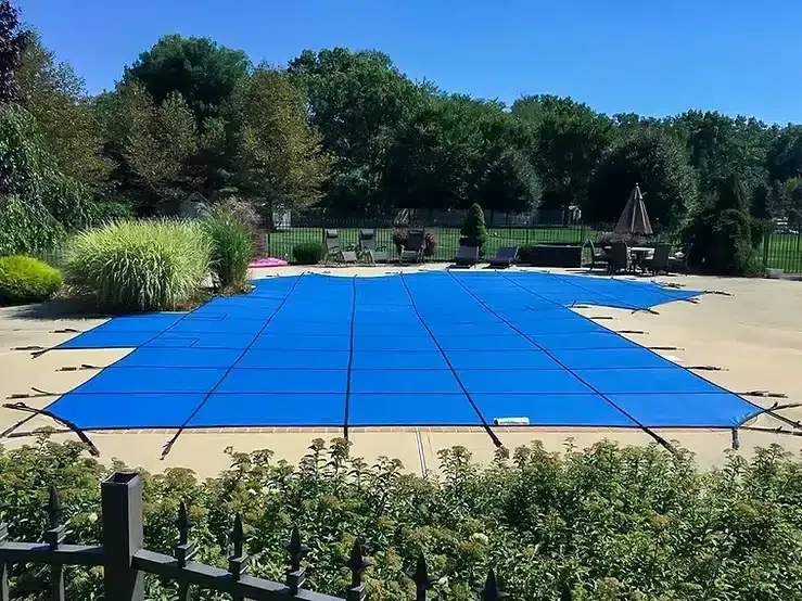 Blue pool cover on an outdoor swimming pool; trees in background.