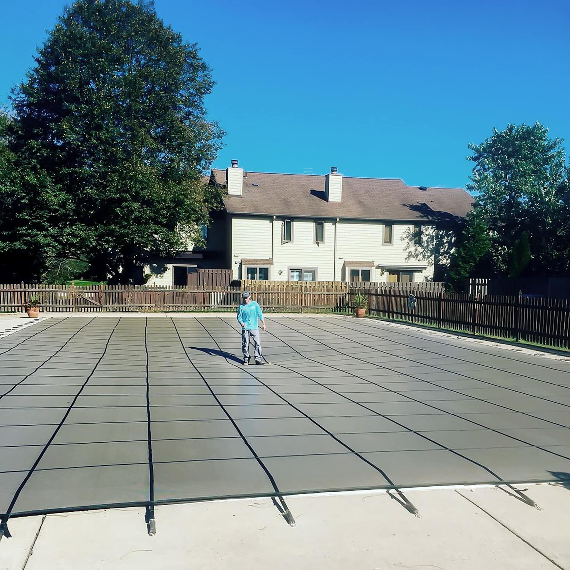 Person standing near a covered swimming pool, background shows houses and clear blue sky.