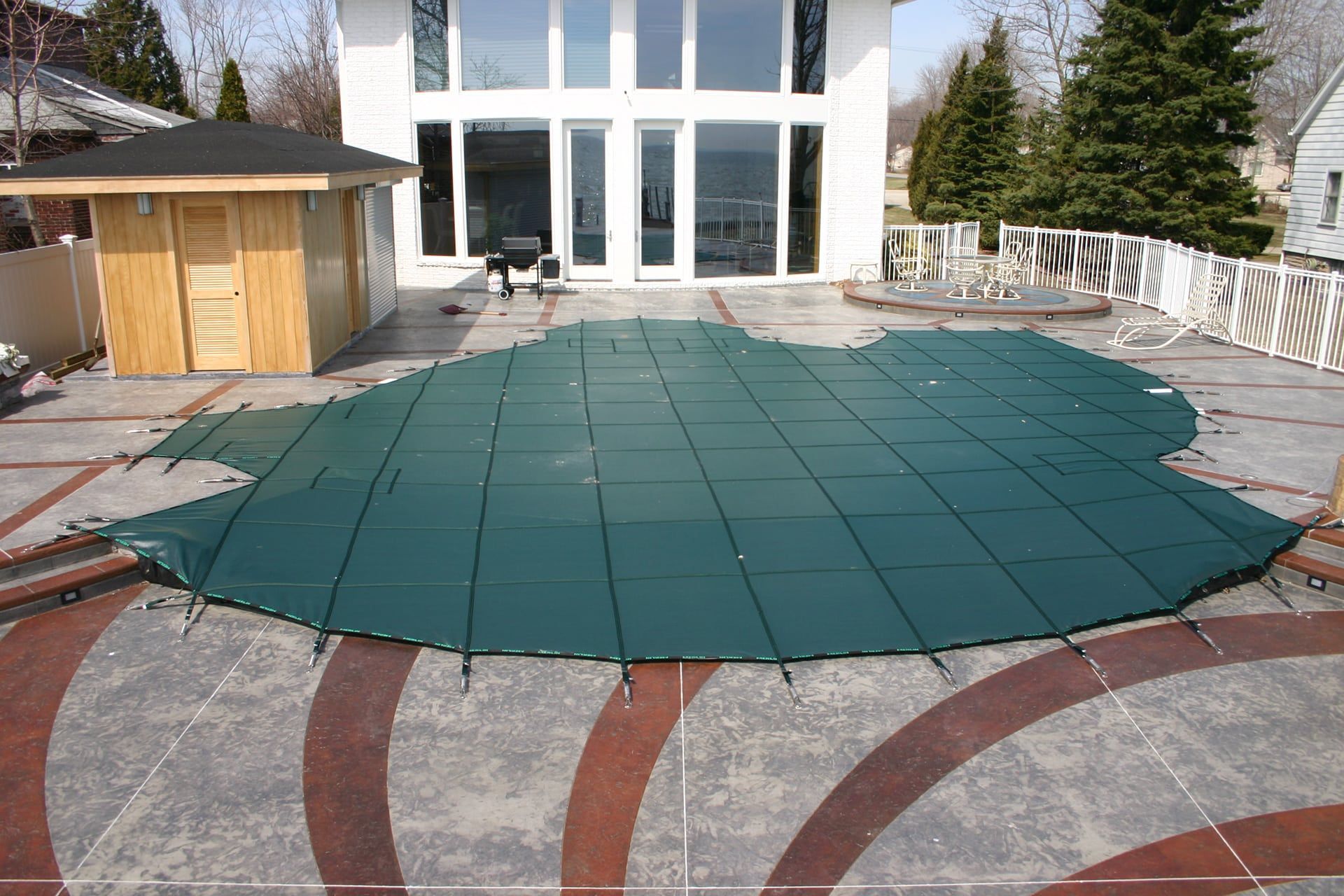 Green pool cover on a stone patio, with a house and gazebo in the background.