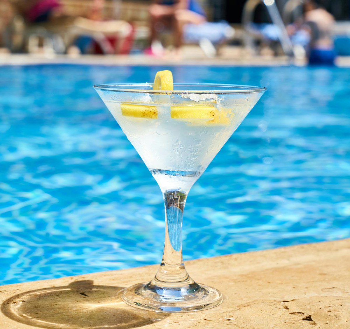 Martini glass with a lemon garnish by a blue swimming pool