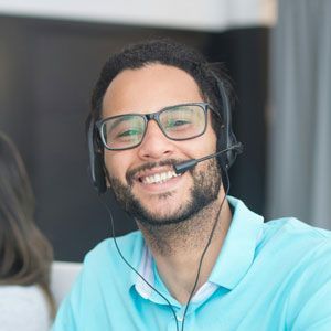 Man with glasses and headset smiles while wearing a blue polo shirt.