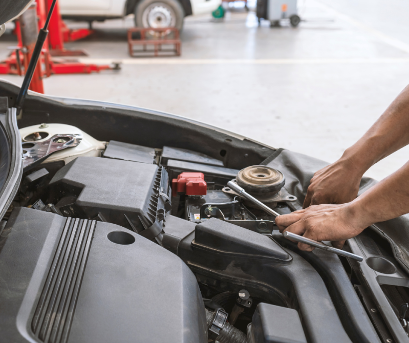 Mani di un meccanico al lavoro all'interno del vano motore di un'auto in un'officina.