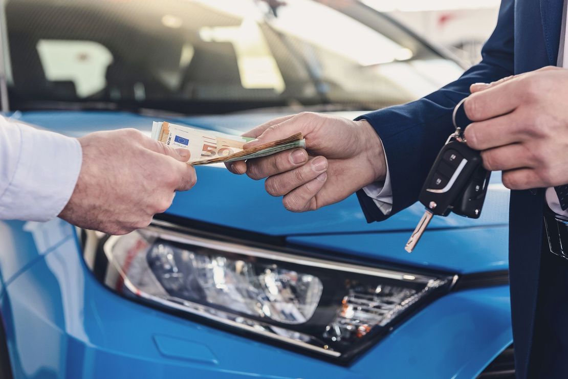 Scambio di chiavi dell'auto e denaro contante davanti a un'auto blu durante una transazione di vendita.