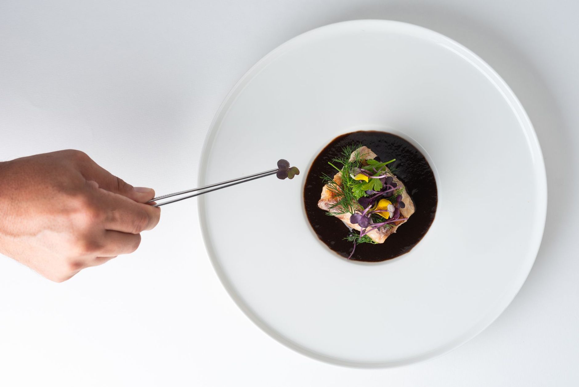 Le chef dispose la garniture sur une assiette. Assiette blanche avec sauce brune et poisson, garnie de fleurs.