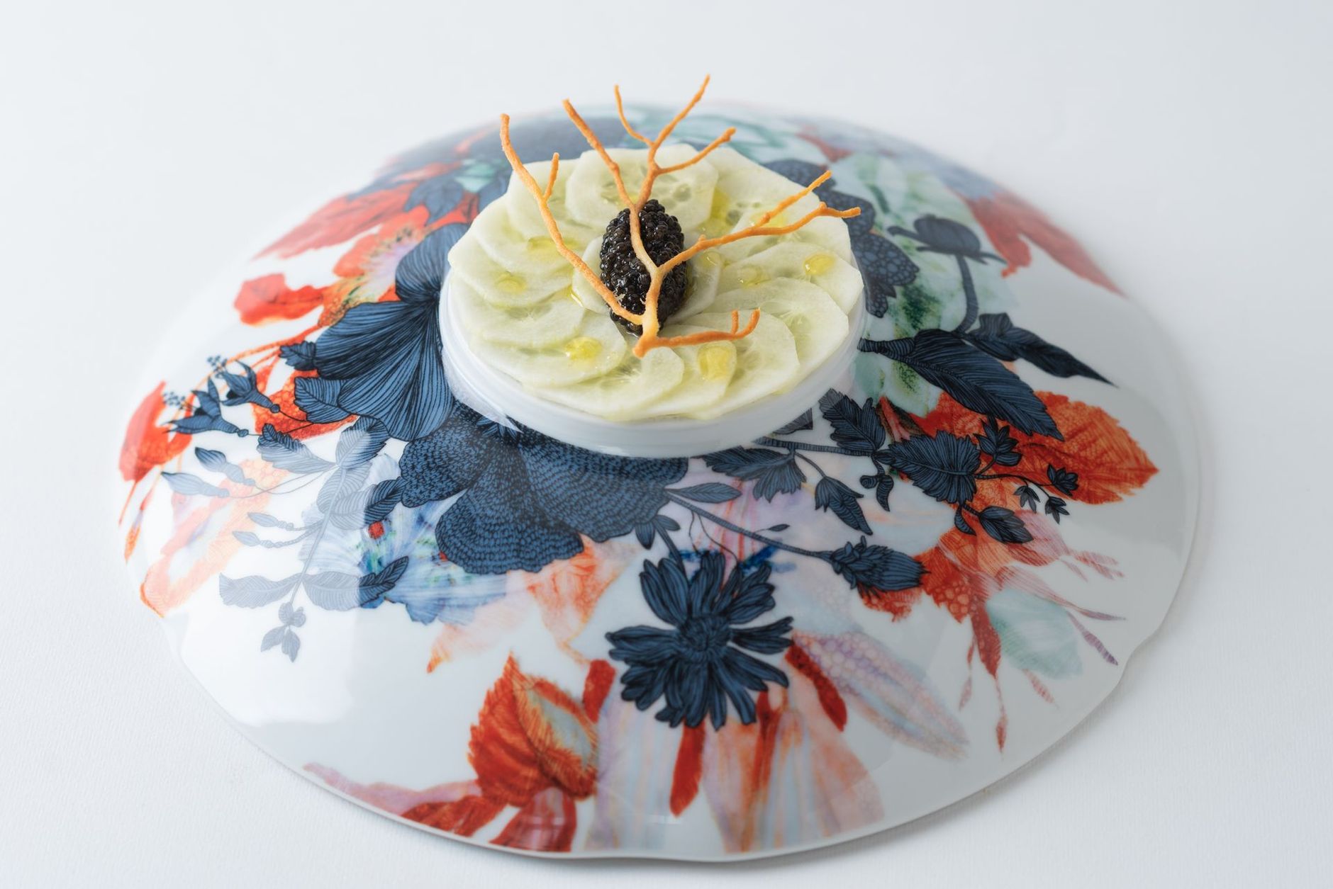 Plat gastronomique présenté sur une assiette à motifs floraux : aliment blanc en couches, garni de caviar.