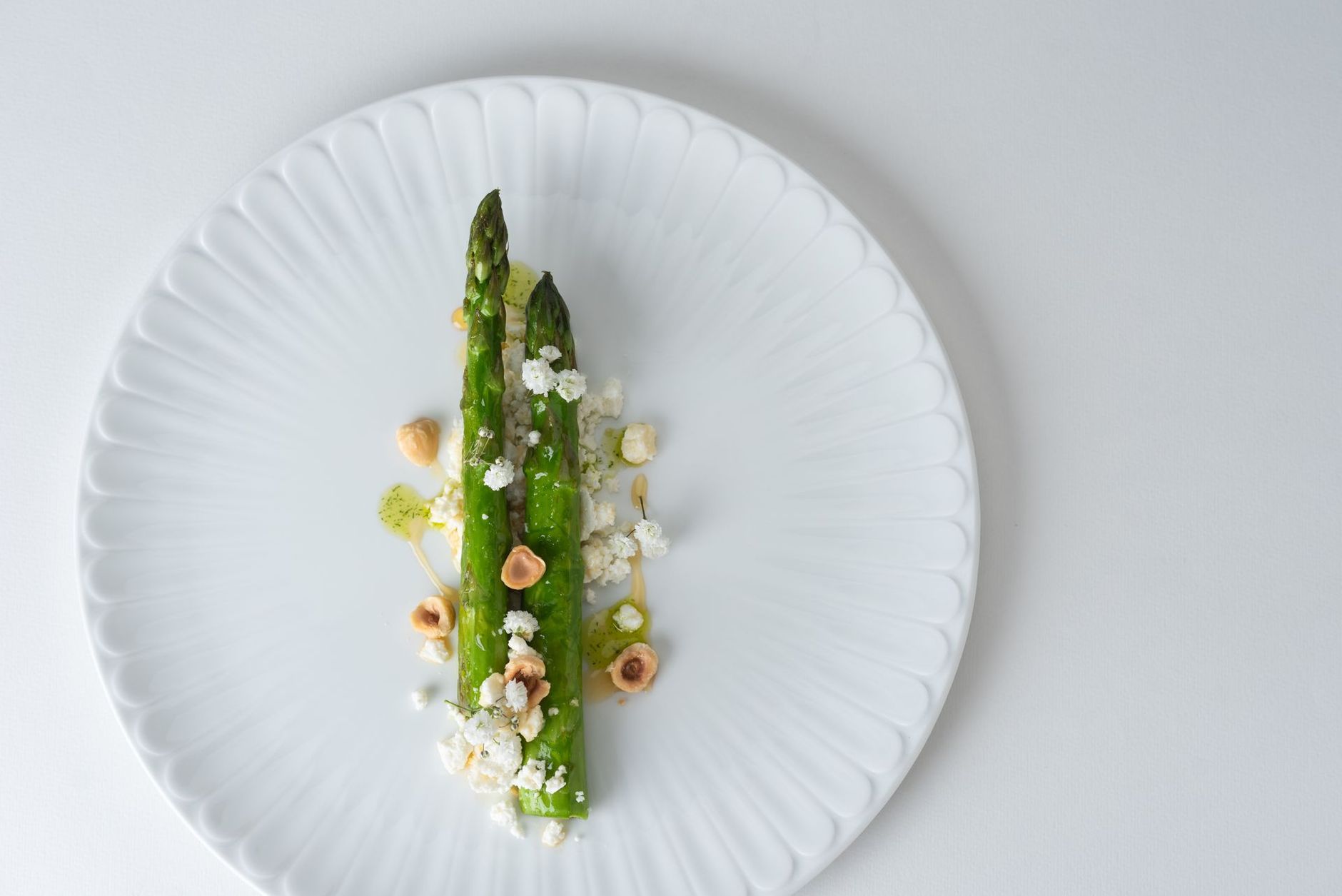 Deux asperges vertes avec des noix et du fromage sur une assiette blanche.