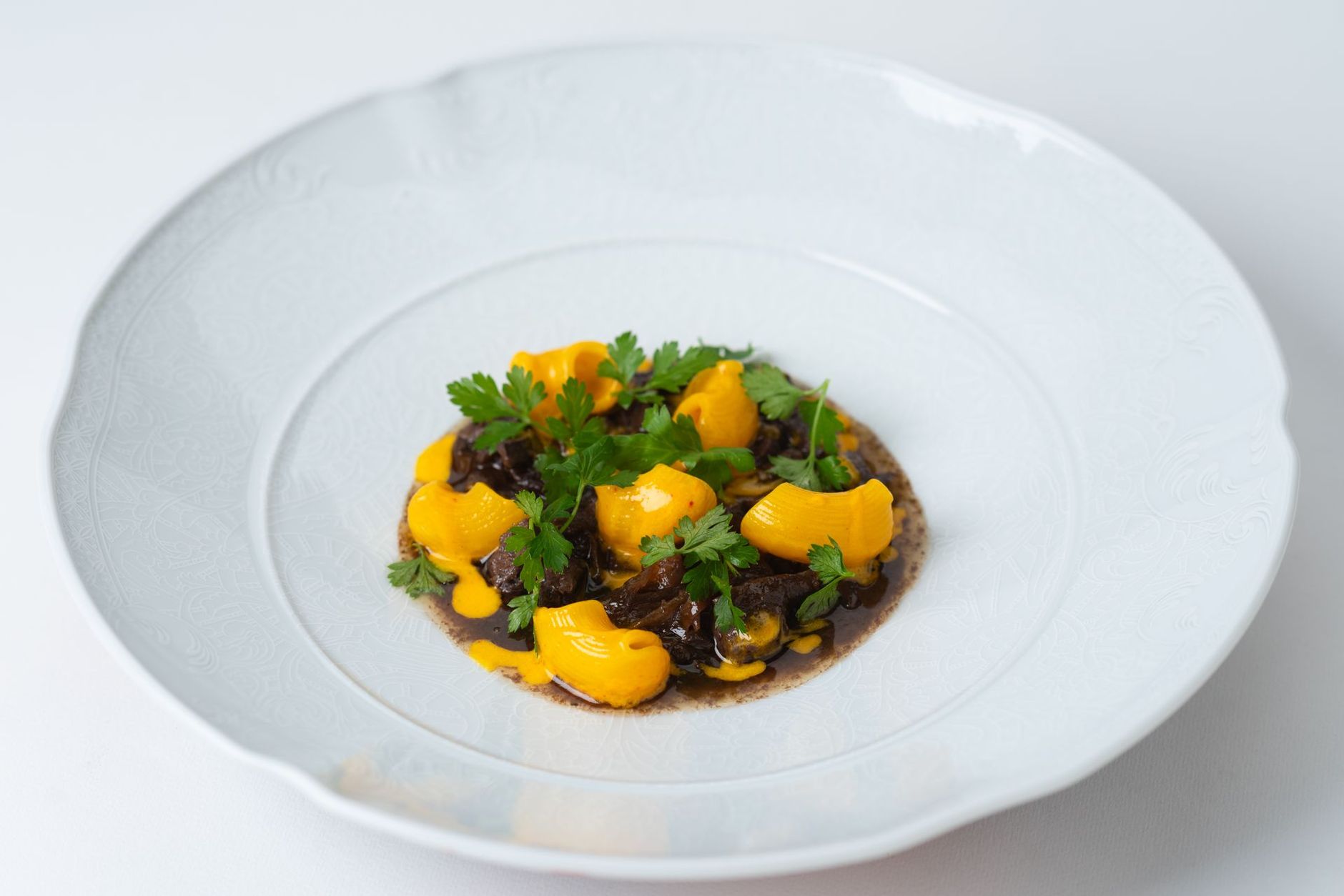 Une assiette blanche avec une sauce foncée, des fruits jaunes et des herbes vertes.