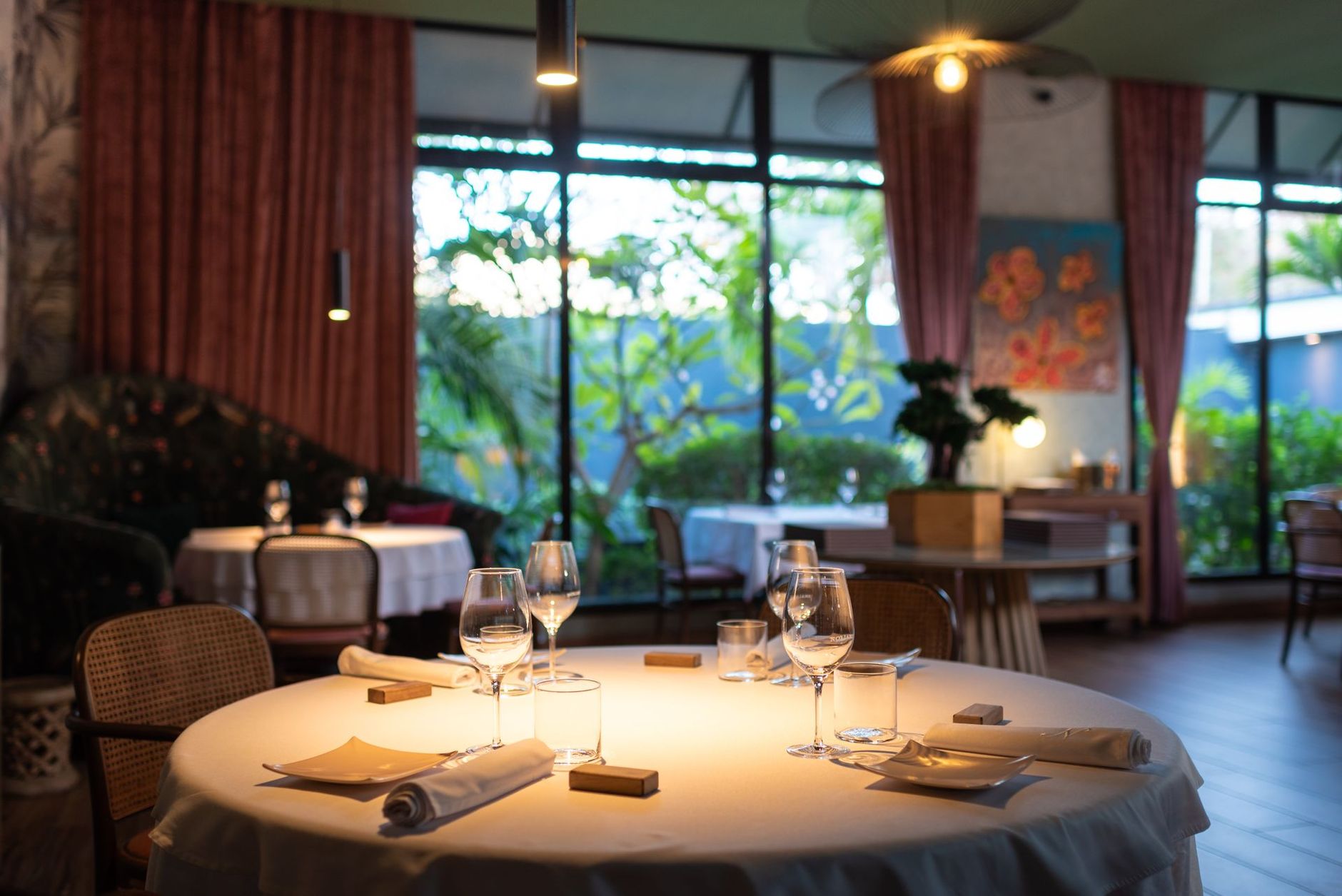 Élégante table de restaurant dressée avec des verres à vin, donnant sur une végétation luxuriante.