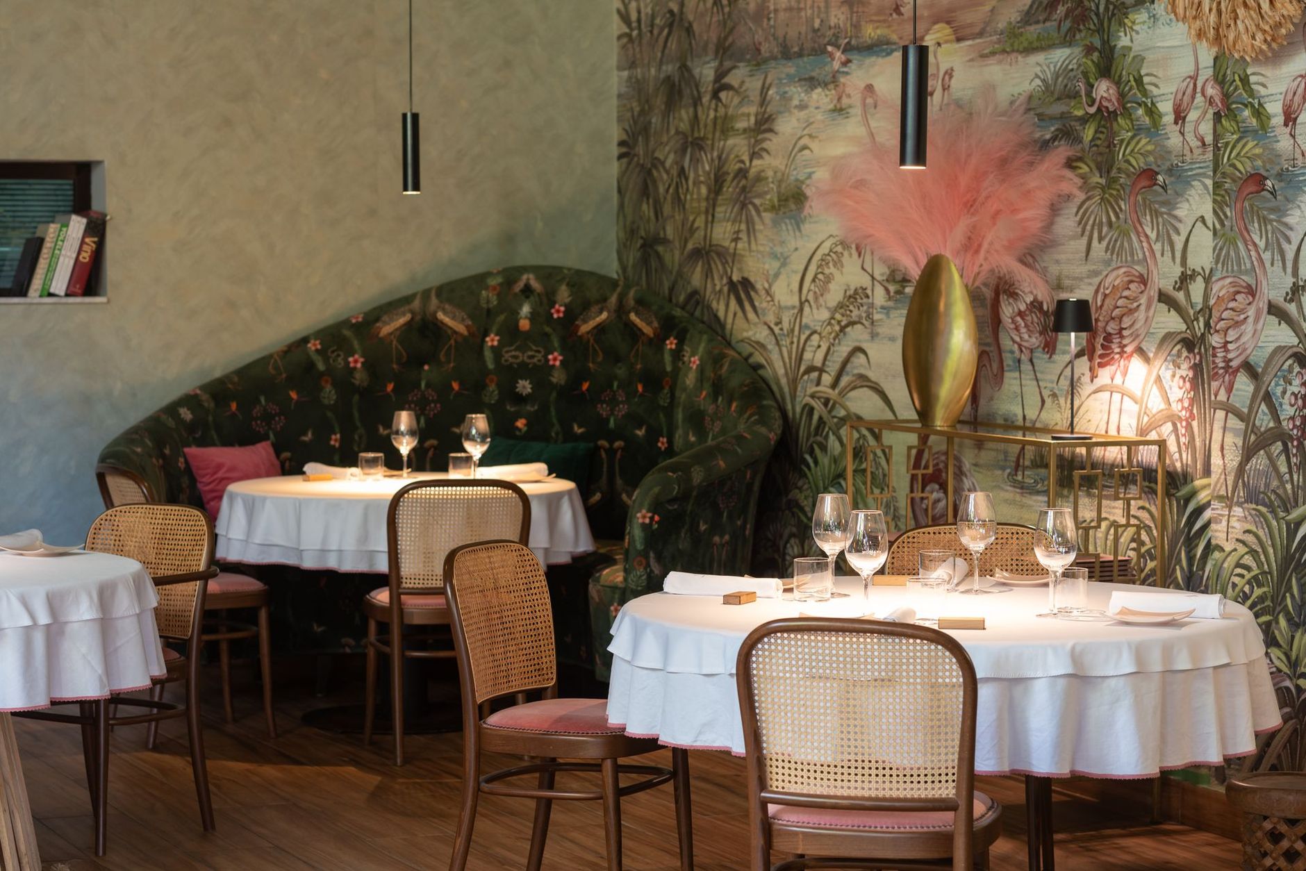 Intérieur de restaurant avec tables rondes, papier peint fleuri et banquettes ornées.