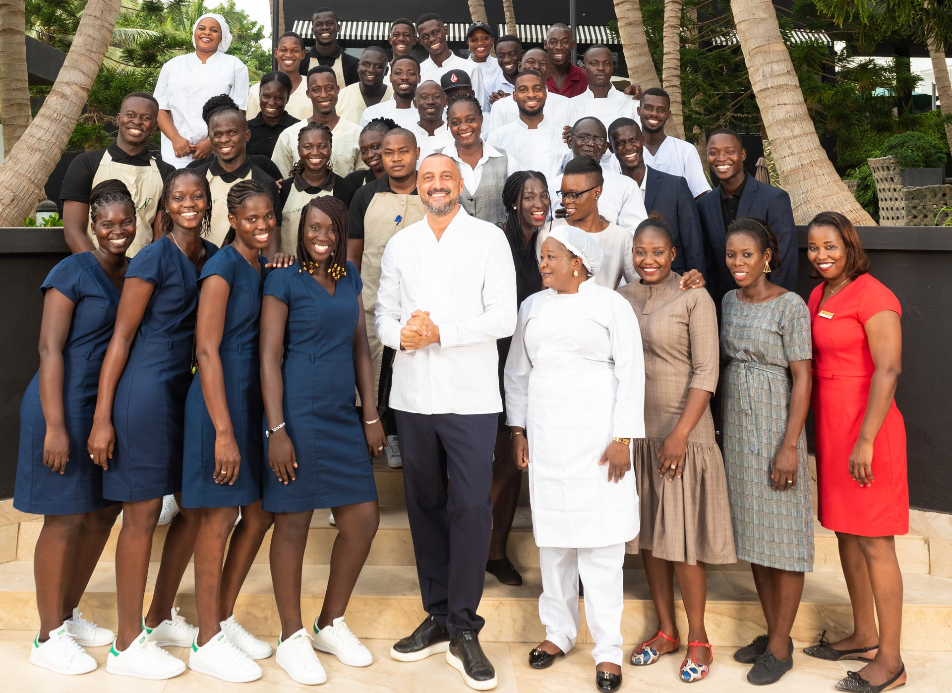 Photo de groupe de personnes, dont beaucoup vêtues de blanc ou de bleu, sur des marches, probablement dans un lieu.