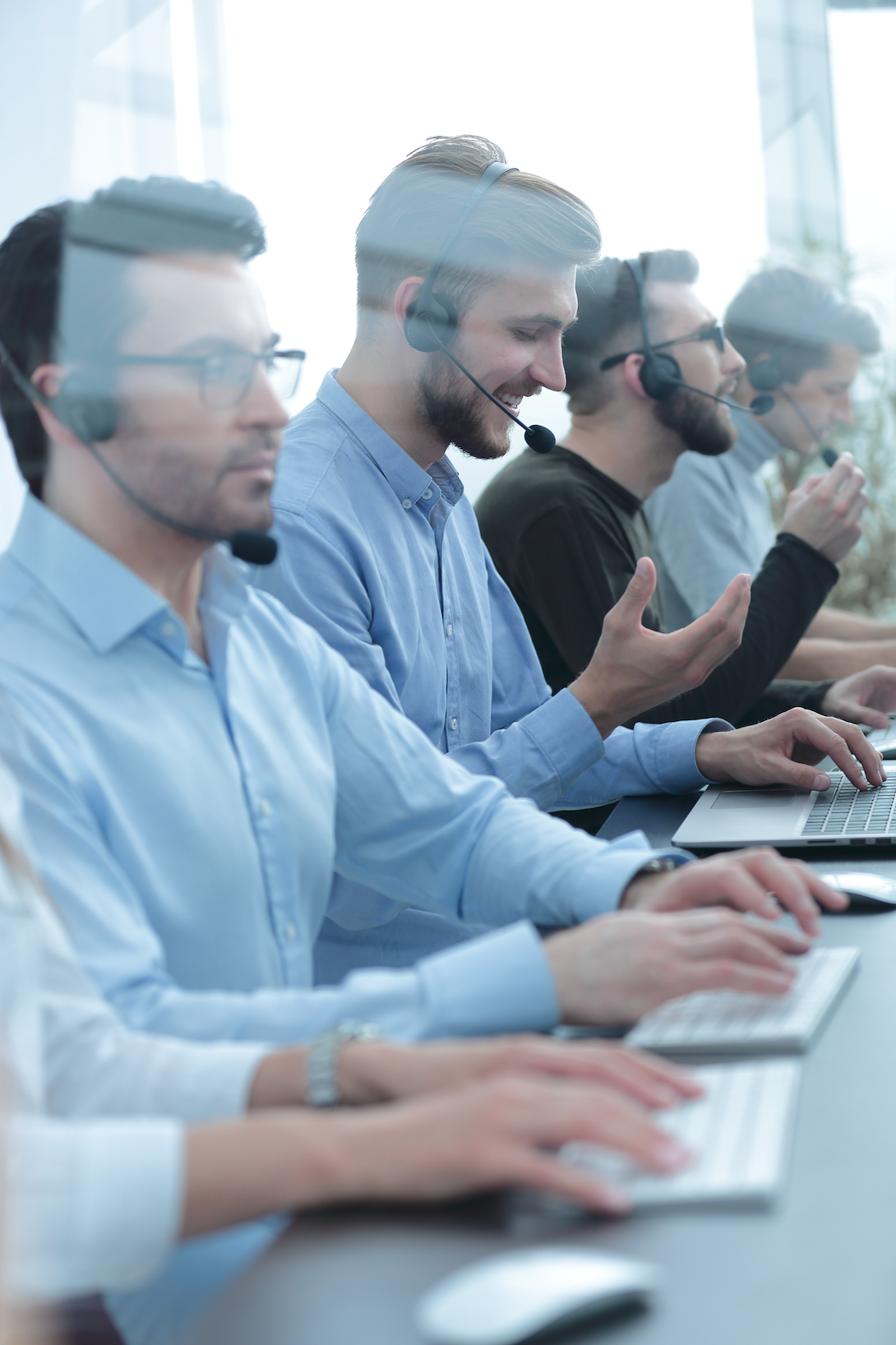 A group of people are sitting in a call center using laptops and headphones.