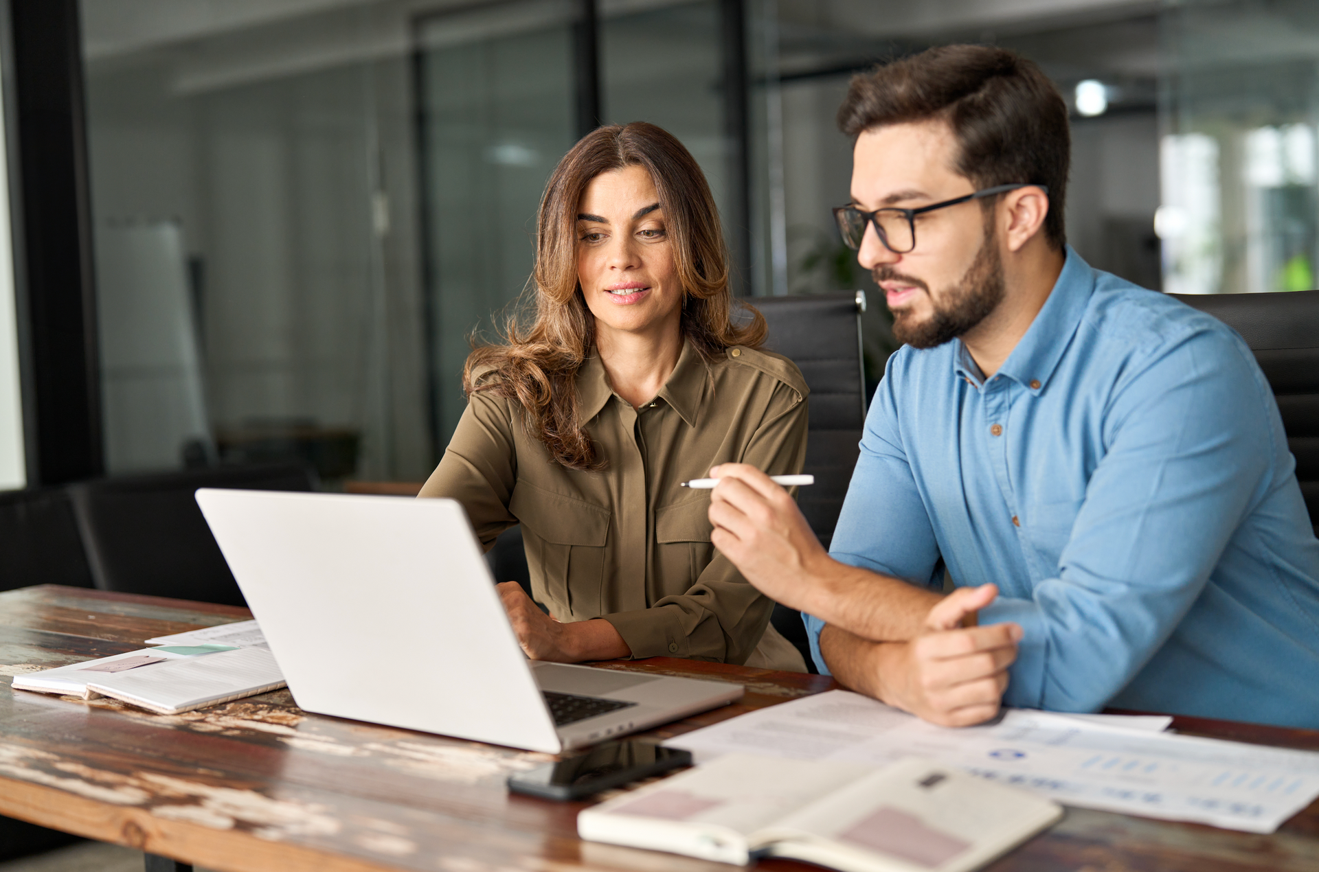 A man and a woman are sitting at a table looking at a laptop computer.
