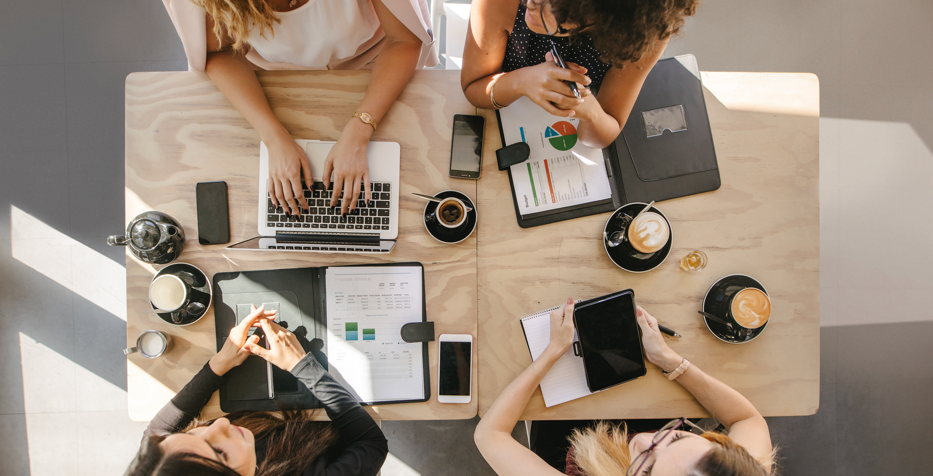 A group of women are sitting around a table with laptops and tablets.