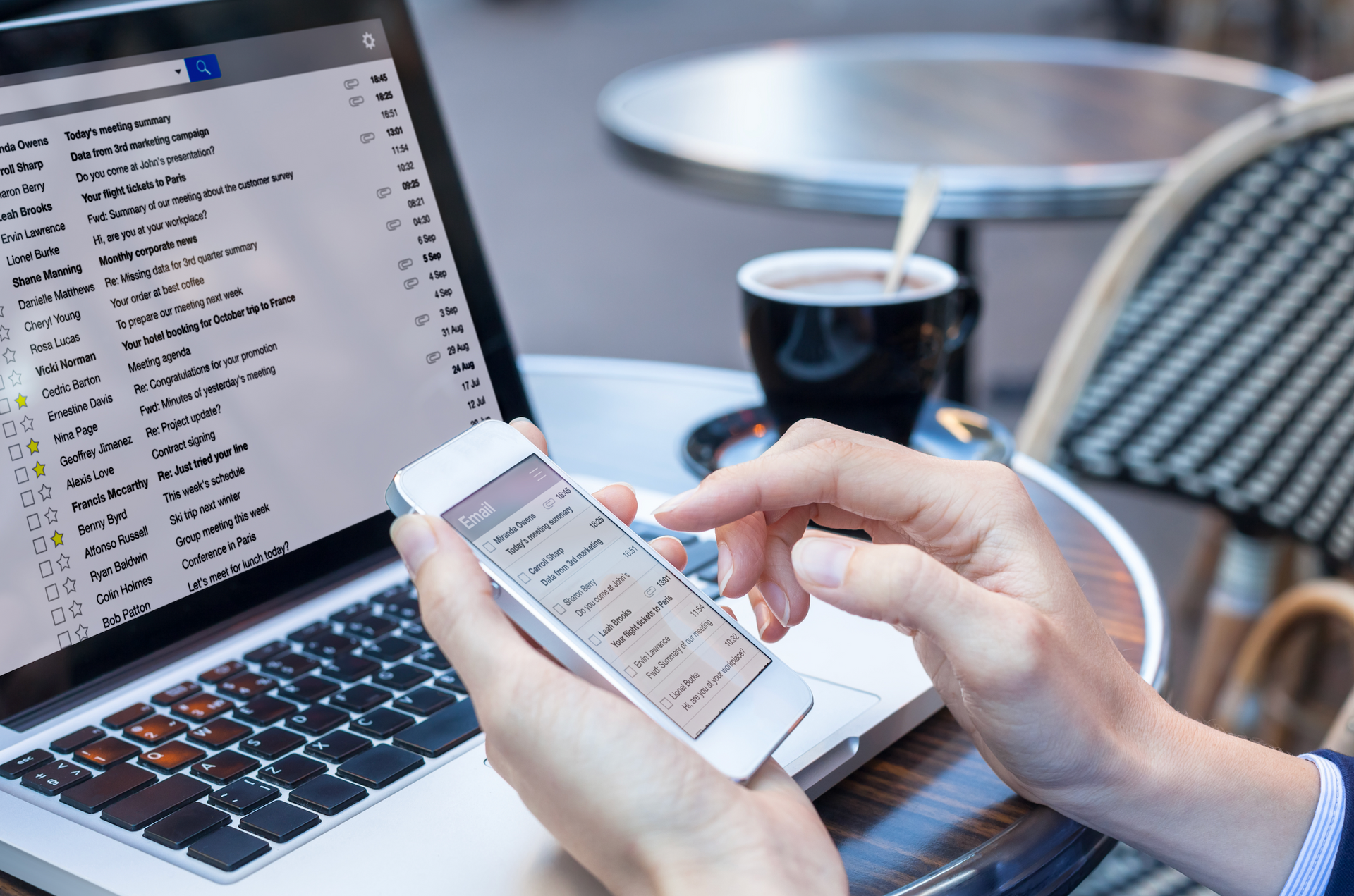A person is holding a cell phone in front of a laptop computer.