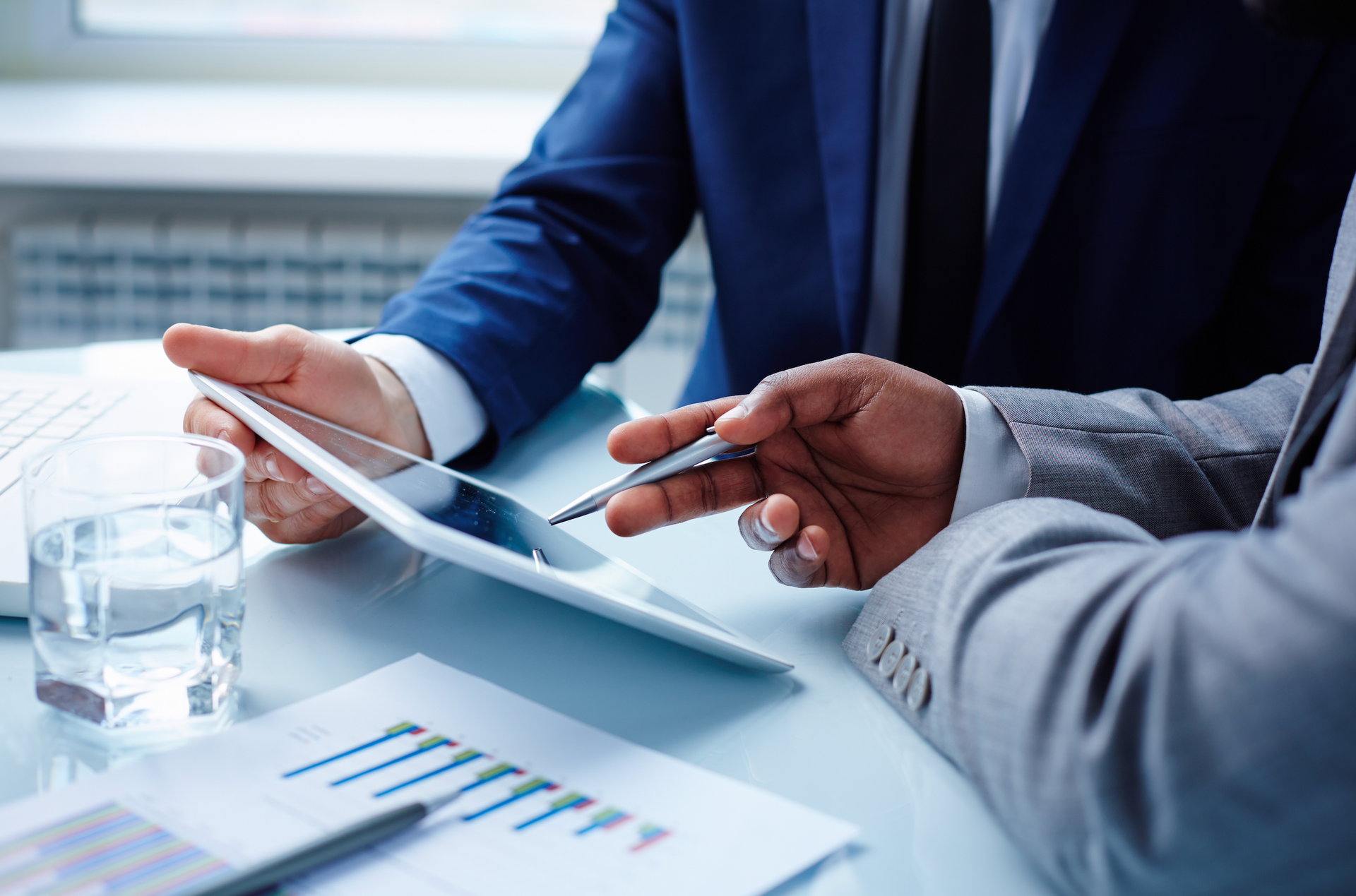 Two businessmen are sitting at a table looking at a tablet.