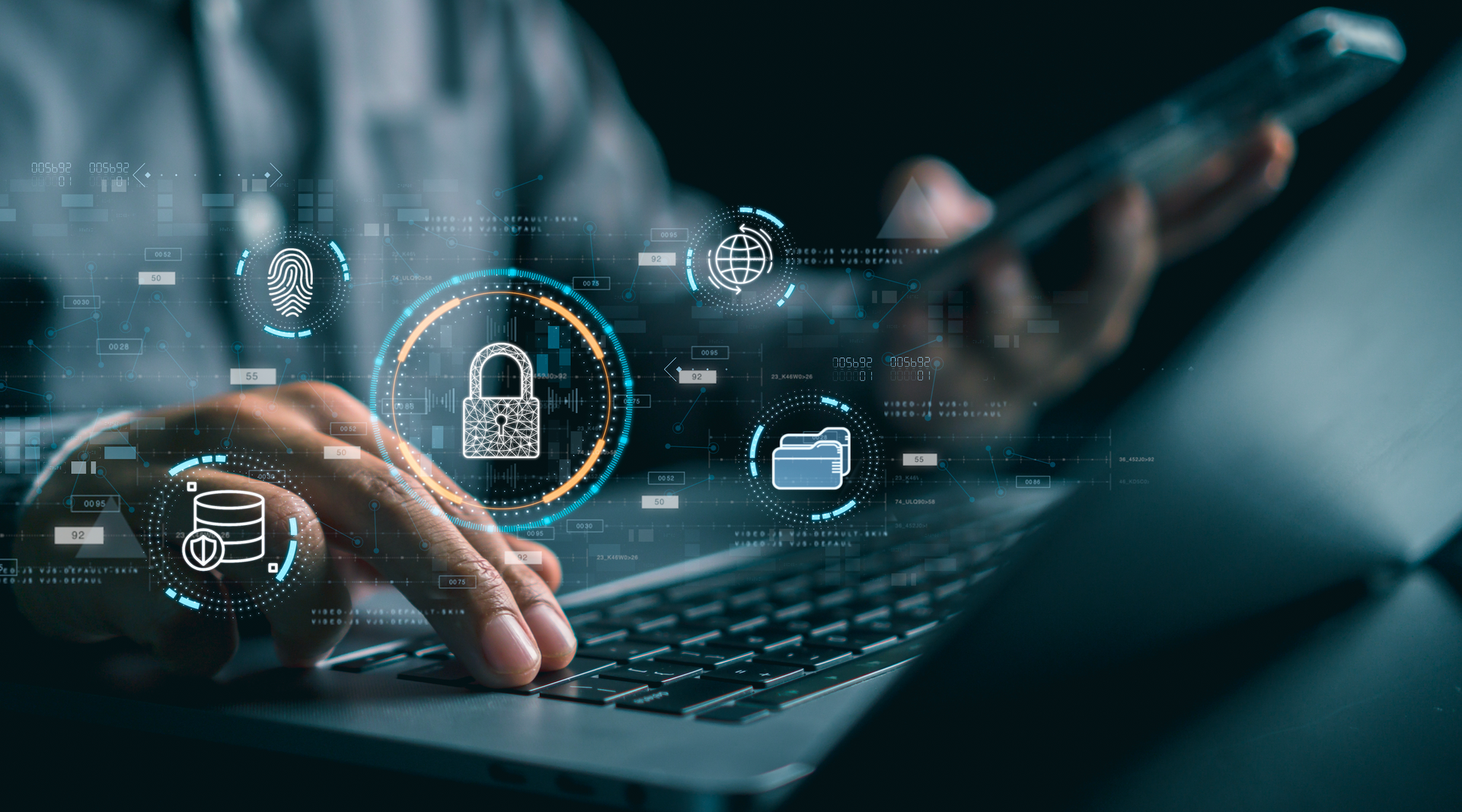 A person is typing on a laptop computer while holding a cell phone.