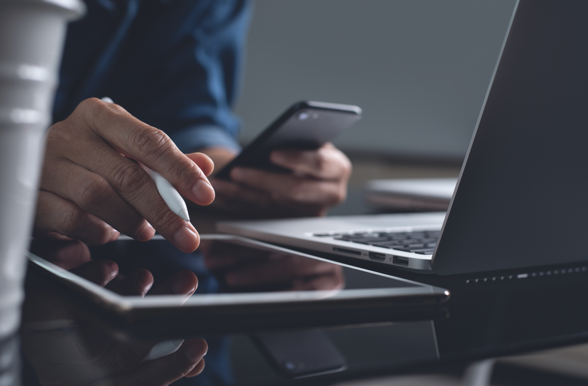 A man is using a tablet and a laptop while holding a cell phone.