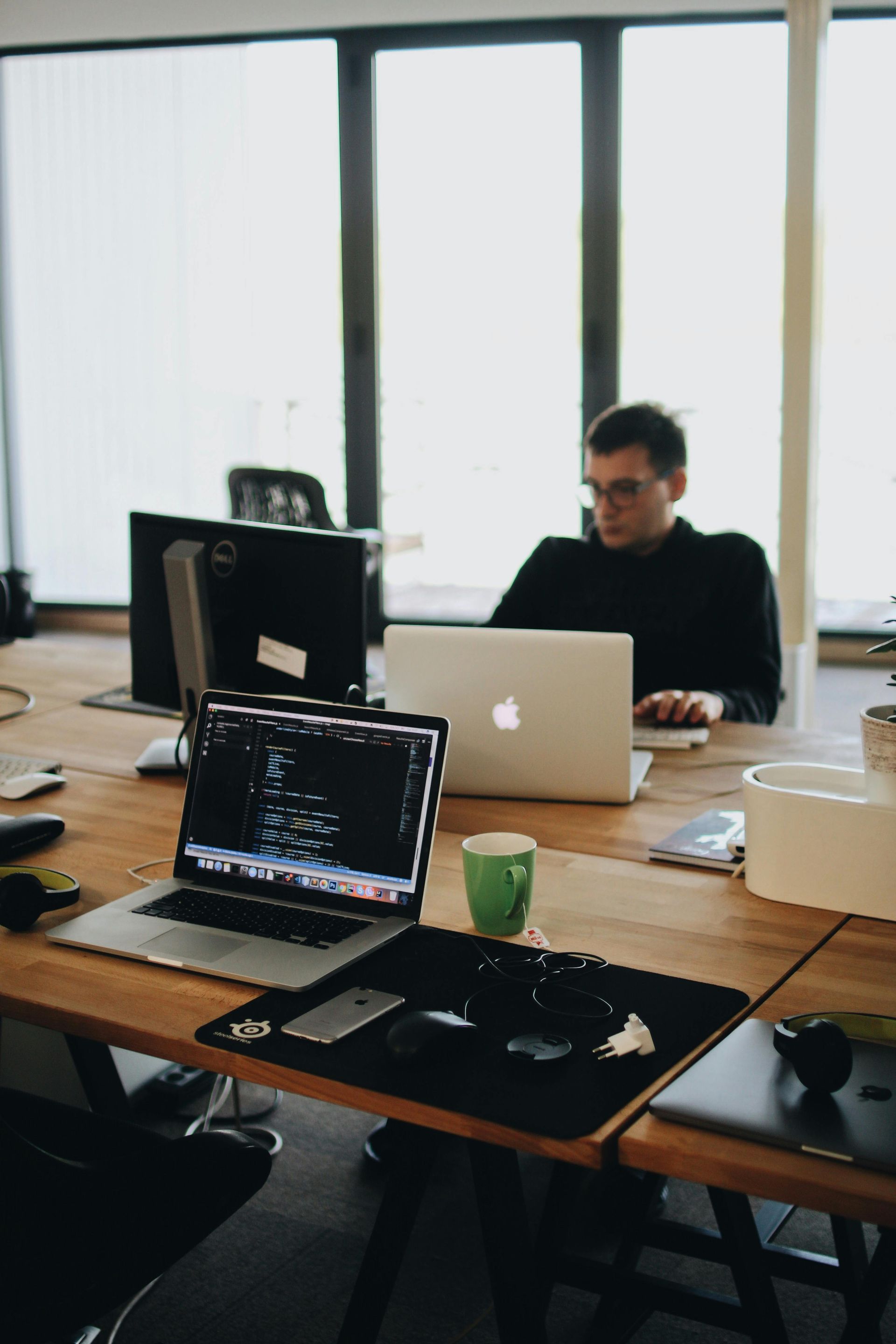 A man is sitting at a desk with two laptops on it.