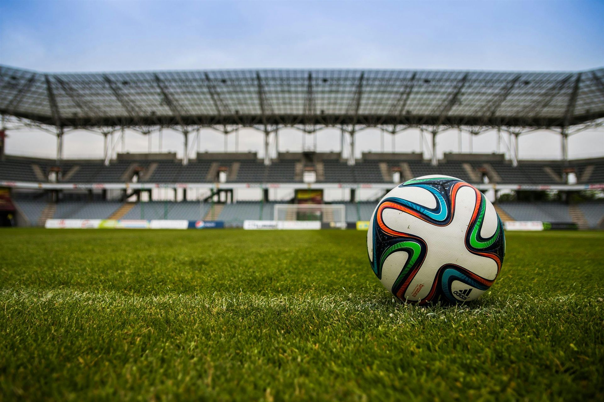 A soccer ball is sitting on the grass in front of a stadium.