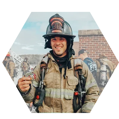 Firefighter in helmet and gear, holding medal, smiling outdoors at a training exercise.