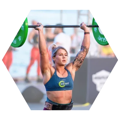 Woman lifting barbell overhead, wearing a blue sports bra, with a tattoo on her arm, in a competition.