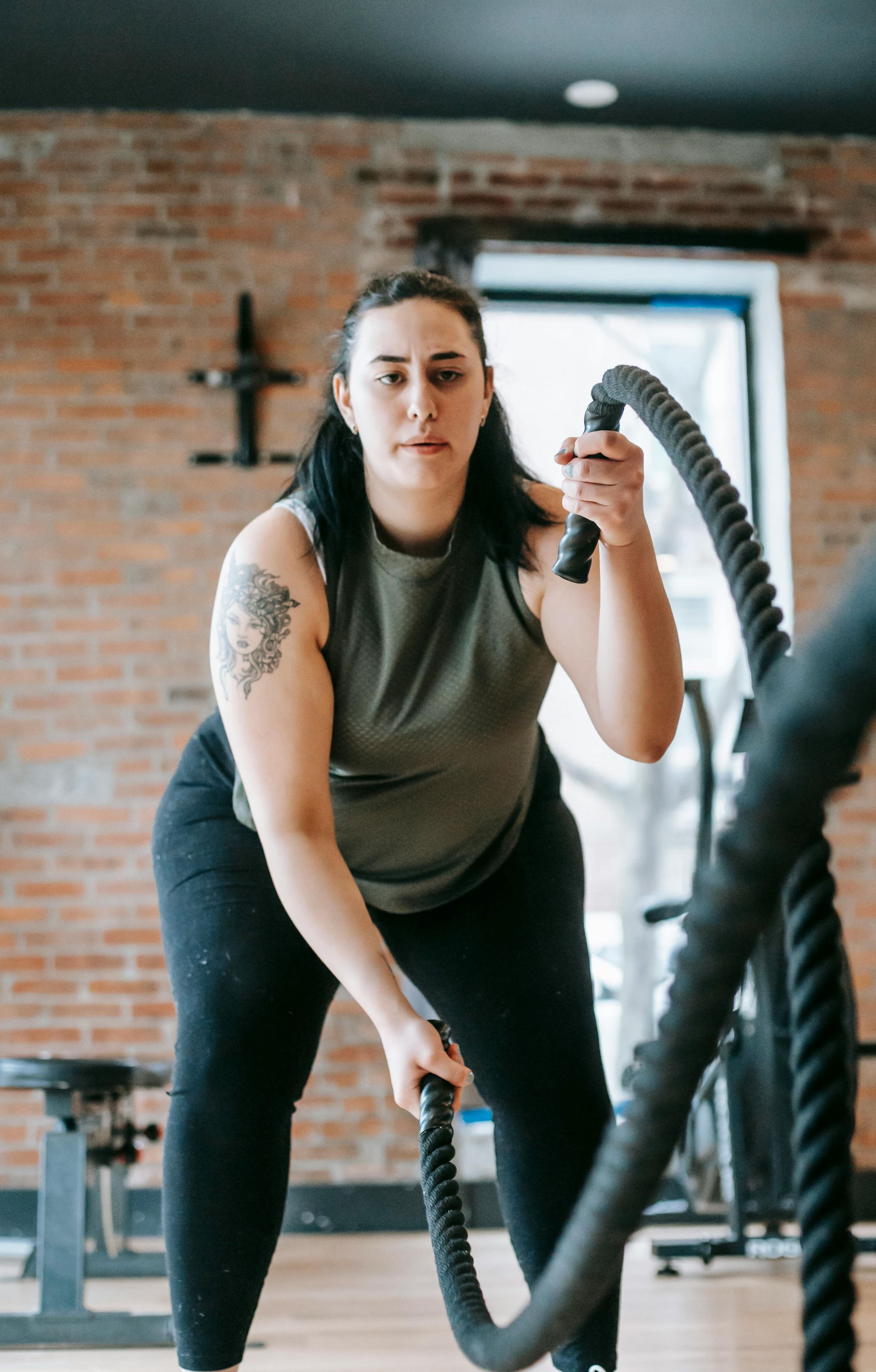 Woman working out with battle ropes in a gym, squatting, focused expression.