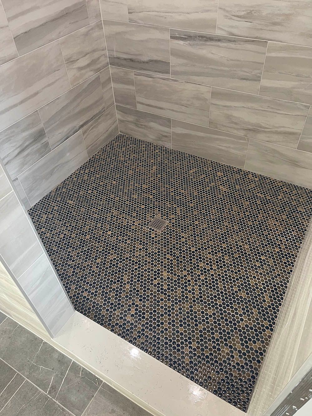 A shower stall with a mosaic tile floor and walls.