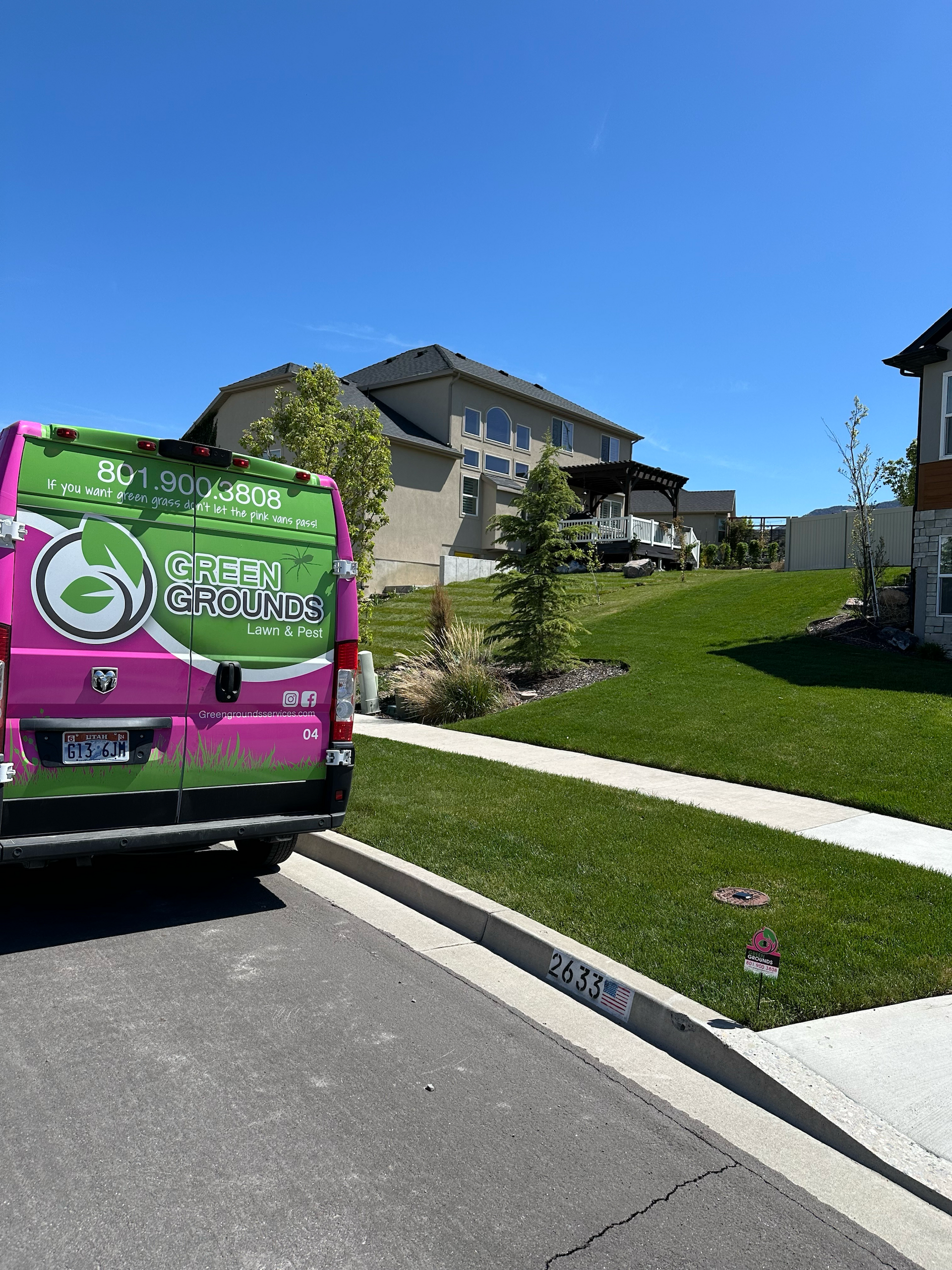 A pink and green van is parked on the side of the road in front of a house.