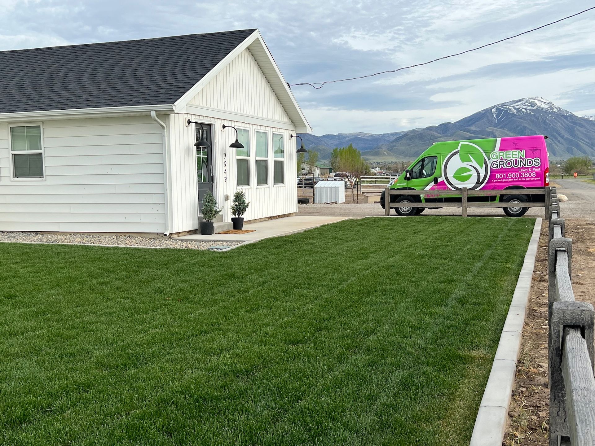 A green and pink van is parked in front of a white house.