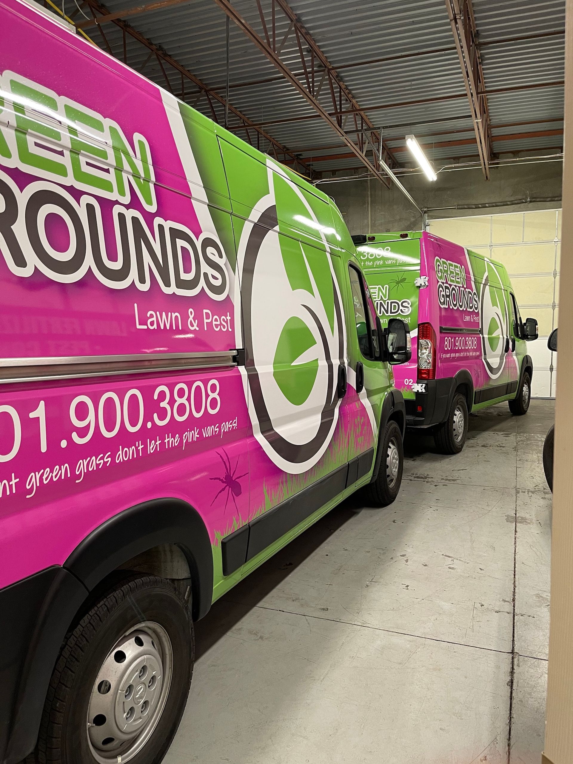 Two pink and green vans are parked next to each other in a garage.