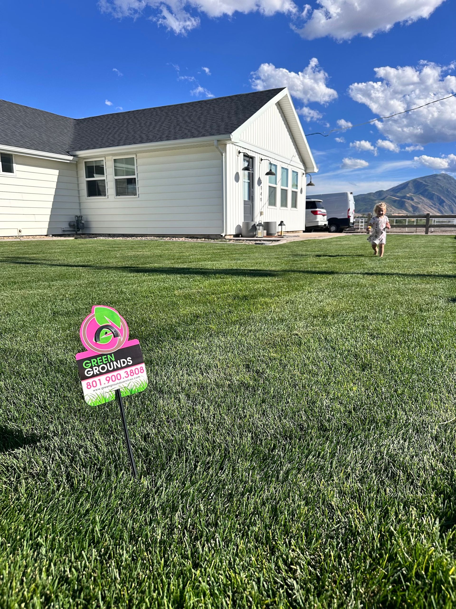 A little girl is standing in front of a house with a sign in the grass.