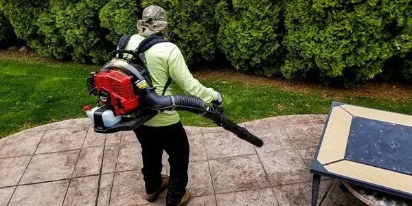 A man is blowing leaves on a patio with a backpack blower.