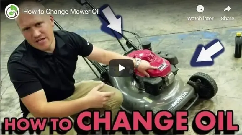 A man is sitting on the ground looking at a lawn mower.