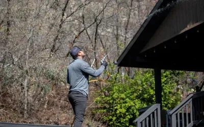 A man is cleaning the gutters of a house with a hose.