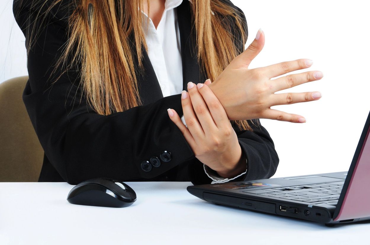Impiegato che si strofina il polso accanto al laptop e al mouse sulla scrivania