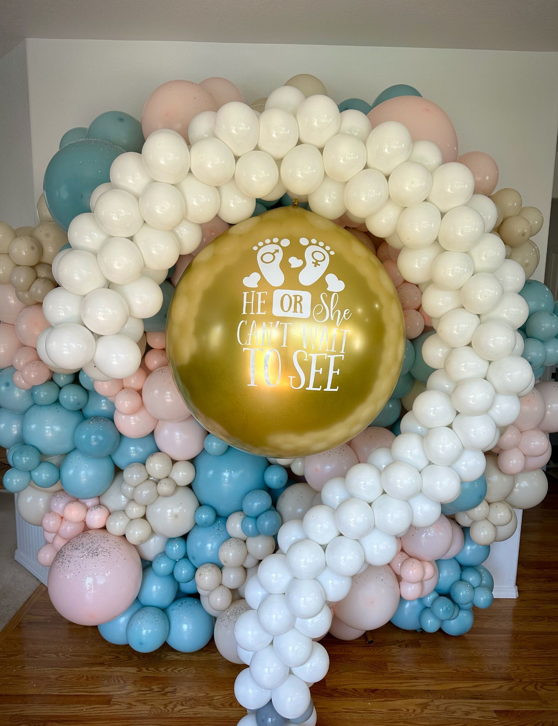 Gender reveal balloon arrangement with gold center balloon and white, blue, and pink balloons.